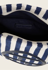 Borsa in tessuto a righe con strisce blu navy e bianche, chiusura con zip e un accento circolare in pelle. Interno foderato con un tessuto scuro a contrasto.