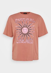 Camiseta oversized de color rosa con un diseño de sol y texto en rosa que dice "Sueños Místicos". Manga corta y cuello redondo.