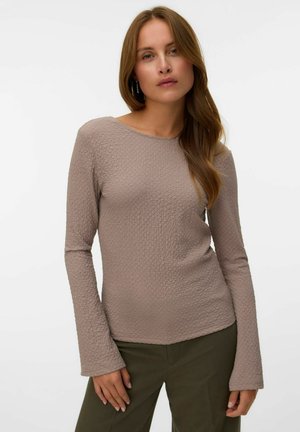Langsleeve, getextureerde top in licht taupe met een ronde hals. Heeft uitlopende mouwen en een fitted silhouet. Gecombineerd met olijfgroene broek.