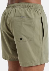 Bañador color caqui con cintura elástica, bolsillos laterales y un bolsillo trasero con un botón negro. Tejido suave con un acabado mate.