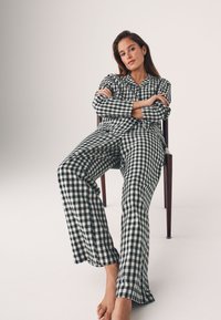 Kockás pizsama szett zöld és fehér színben, gombos felsővel és laza szabású nadrággal, puha anyagból készült; nincsenek látható minták vagy részletek.