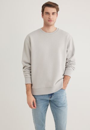 Hellgrauer Sweatshirt mit rundem Halsausschnitt und gerippten Bündchen, kombiniert mit hellblauen Jeans. Der Stoff wirkt weich und angenehm zu tragen.