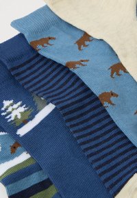 Τέσσερις ζεύγη πολύχρωμων παιδικών κάλτσων με μοτίβα που περιλαμβάνουν αρκούδες, ρίγες και χιονισμένα δέντρα, τοποθετημένα επικαλυπτόμενα σε λευκό φόντο.