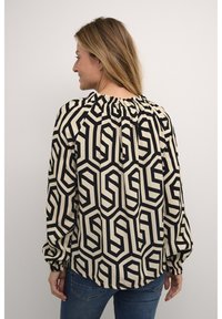 Blusa nera e crema con motivo geometrico, scollatura elastica arricciata e maniche lunghe a sbuffo, abbinata a jeans.