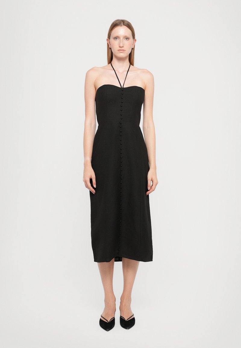 Black strapless dress with a fitted bodice, full skirt, and a row of buttons down the front. Smooth fabric, midi length, paired with black heels.