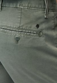 Pantalons khaki avec une finition texturée, dotés d'une poche arrière à rabat, d'une fermeture à bouton et d'une broderie discrète du logo noir au-dessus de la poche.