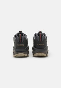 Black and grey sneakers with a textured upper, cushioned sole, and a patterned pull tab featuring orange accents and "SKECHERS OUTDOOR" branding.