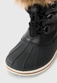 Stivale impermeabile nero con punta rotonda, suola in gomma e colletto in pelliccia sintetica. Include un design con lacci e occhielli in metallo, insieme a dettagli di cucitura.