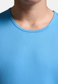 Modrá košeľa s krátkym rukávom, s hladkou a pružnou textúrou a okrúhlym výstrihom. Tkanina má jemný ryhovaný vzor.