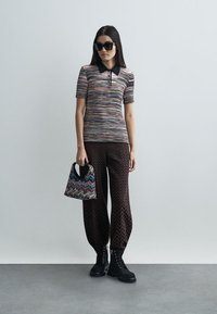 Πλεκτό πόλο μπλουζάκι με πολύχρωμες ρίγες, μαύρο γιακά; καφέ πουκαμισέ με σχέδια και φαρδιά πόδια; μικρή τσάντα με μοτίβο; μαύρες μποτάκια με κορδόνια.