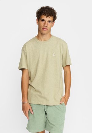 Lys beige bomulds T-shirt med rund hals, korte ærmer og et lille grafisk motiv på brystet, parret med lys grøn shorts.