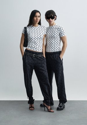 Balti T-krekli ar īsām piedurknēm un melnu pusmēness dizainu, kombinēti ar melnām rakstainām skrējbiksēm. Aksesuāru komplektā ir melna soma un oversized saulesbrilles.