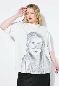 Bílý oversized tričko s černobílým grafickým potiskem ženy v brýlích. Hladká tkanina, volný střih, krátké rukávy.