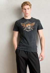 Melns, īsām piedurknēm t-krekls, kas izgatavots no mīksta auduma ar nolietotu apdari. Priekšējā grafikā ir attēlots skelets, spārni un motociklu teksts.