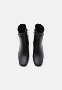 Ζεύγος μαύρων δερμάτινων μποτάκια αστραγάλου με πλαϊνά φερμουάρ, τετράγωνα μύτη και λείο φινίρισμα, φωτογραφημένα από πάνω σε λευκό φόντο.