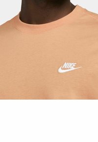 Ljus persikofärgad bomullströja med rund hals och korta ärmar. Har en vit broderad Nike-logga på bröstet. Mjuk textur.