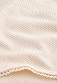 Ribbed béžová látka s jemnou texturou, zdobená jemnou krajkovou lemovkou podél okraje. Měkký a hladký vzhled.