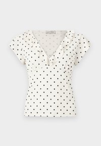 Λευκή μπλούζα με κοντά μανίκια και μαύρες πουά, ντεκολτέ V και βολάν κατά μήκος του γιακά.