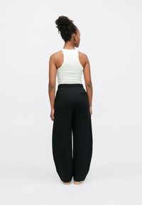 Juodos plačios kojinės kelnės su elastiniu liemeniu, derinamos su balta tankine. Audinys atrodo minkštas ir lygios tekstūros.