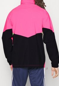 Farvet blokeret jakke med pink, sort og et strejf af neon grøn, med høj krave og en løs pasform. Glat stof, lange ærmer.