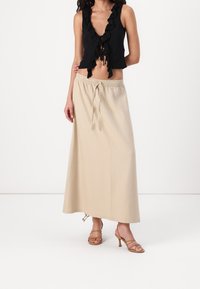 Top corto negro con volantes, escote en V profundo y lazo en la parte delantera, combinado con una falda maxi beige con cintura elástica y cordón.