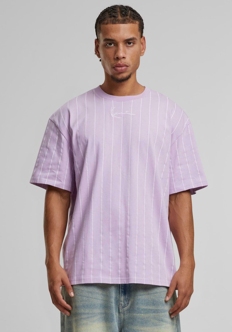 T-shirt oversized en lavande avec des rayures verticales blanches et un petit logo sur la poitrine. Matière en coton, manches larges et col rond.