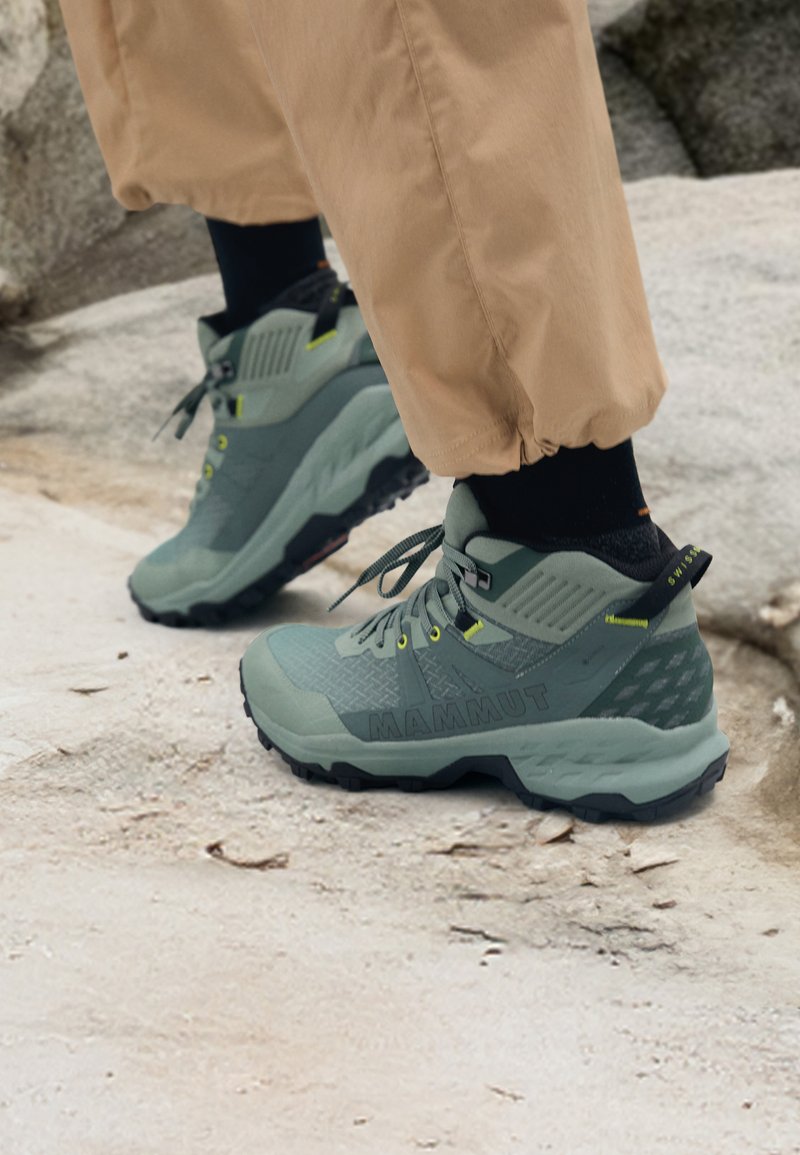 Scarpe da esterno Mammut in verde spento con tomaia testurizzata, dettagli gialli e suola nera robusta. Design durevole per le attività all'aperto.
