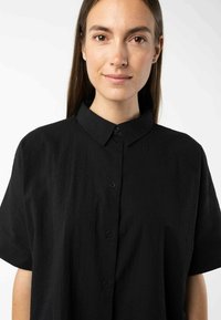 Zwarte shirt met korte mouwen van een gestructureerde stof, met een knoopsluiting aan de voorkant en een klassieke kraag. Glad oppervlak met subtiele details.