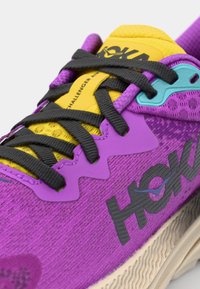 Lilla joggesko med en teksturert stofføvre, svarte snørebånd, gul tunge, lyseblå detaljer og en beige gummisåle.