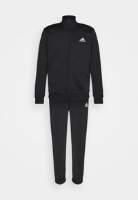 Survêtement Adidas noir avec veste zippée intégrale et pantalon assorti, arborant les logos blancs Adidas sur la poitrine et la cuisse, présenté sur un fond uni.