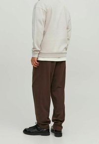 Sudadera gris claro con un corte relajado, combinada con pantalones marrones sueltos. Unos zapatos negros de cordones completan el atuendo. Se puede apreciar la suave textura de la tela.