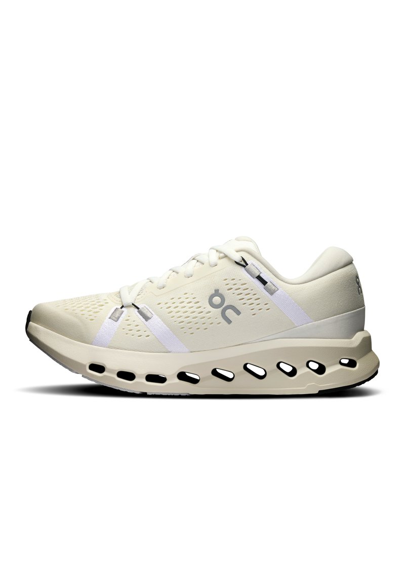 Chaussure de course crème clair avec une tige texturée, accents blancs et une semelle rembourrée dotée d'ouvertures pour la respirabilité.