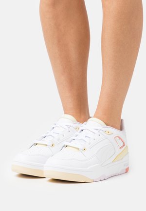 Weiße Sneaker mit glattem Lederfinish, goldenen Akzenten, gepolsterten Kragen und einem flachen Design. Details in Pastellrosa und Orange.