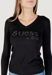 Maglione nero a maniche lunghe con scollo a V e logo ricamato "Guess". Presenta una vestibilità aderente e una texture morbida.