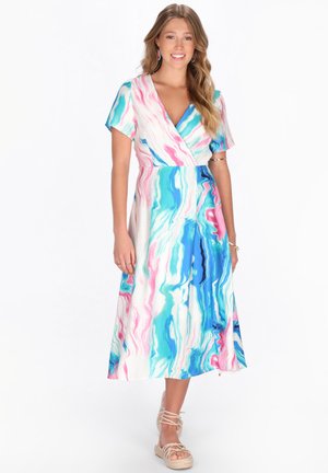 Donna sorridente che indossa un vestito midi a maniche corte con scollo a V, decorato con motivi astratti a marmo blu, rosa e bianco, e sandali beige con lacci.