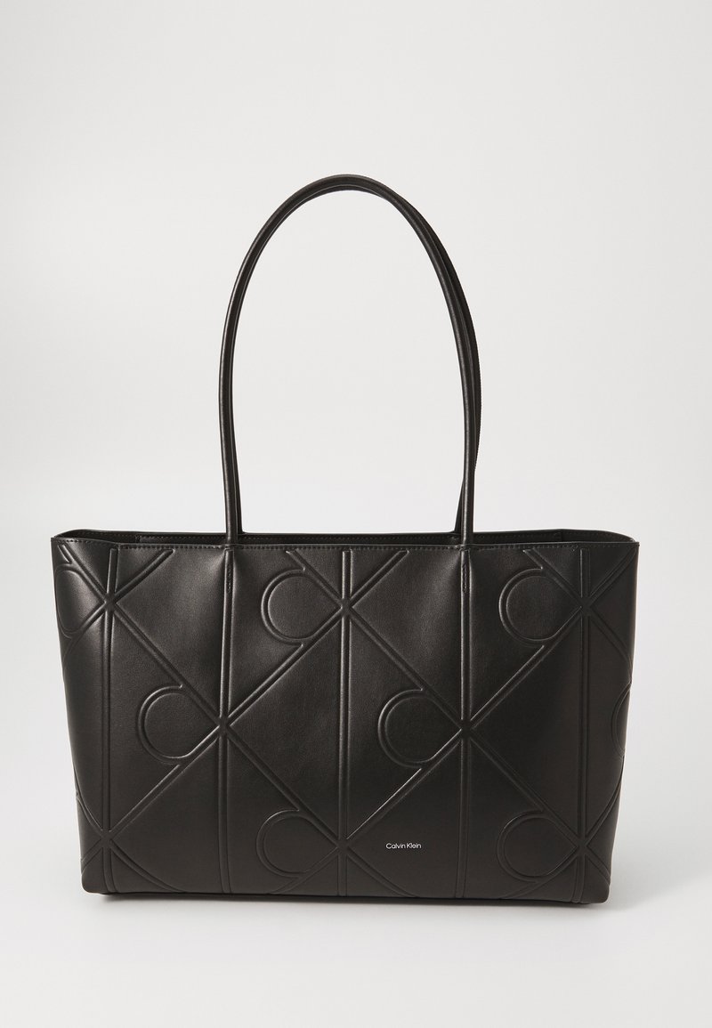 Zwarte lederen tote bag met gegraveerde geometrische patronen, uitgerust met twee lange handvaten en een merklogo aan de onderkant. Ruimtelijk ontwerp.
