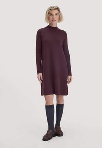 Bordeaux farbenes Strickkleid mit hohem Kragen und langen Ärmeln, kombiniert mit kniehohen, gerippten Socken und braunen Loafers. Glatte Textur, knielang.