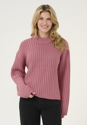 Pink knitted sweater with a high collar, ribbed texture, and wide sleeves, paired with black pants.