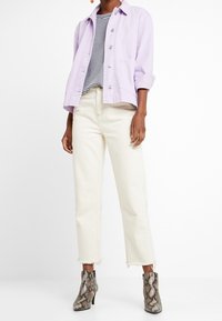 Giacca corta lilla con maniche arrotolate, top a righe bianco e nero, jeans dritti avorio e stivali alla caviglia con stampa pitone.