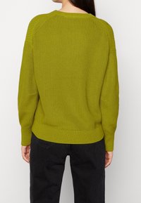 Grüner Strickpullover mit Rippstruktur, runder Ausschnitt, langen Ärmeln und seitlichen Schlitzen. Saum am unteren Ende leicht tailliert.