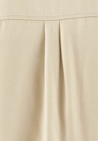 Tissu beige clair présentant un design plissé avec une texture lisse et un éclat subtil. Ourlet surpiqué le long du bord supérieur.