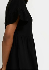 Svart klänning med korta volangärmar och en figurnära bodice med ett flödande nederdel. Tyget ser mjukt och slätt ut med en enfärgad design.