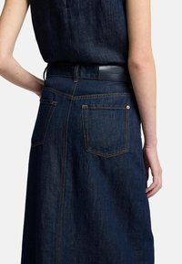 Jupe en denim bleu foncé avec une taille ajustée, poches arrière et coutures en contraste. Texture lisse et design en A s'étend jusqu'au mollet.