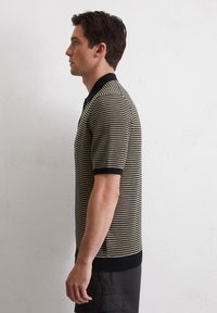 Korte mouwen polo shirt in gestreepte zwart en beige tricot. Kenmerkt zich door een zwarte kraag, ribgebreide manchetten en zijsplitten aan de onderkant.
