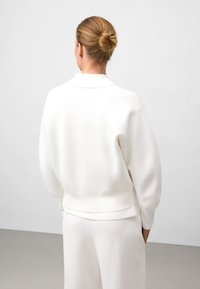 Pull en maille blanc texturé avec une coupe décontractée, doté d'un col et d'un ourlet côtelé. Porté avec un pantalon assorti, ample.