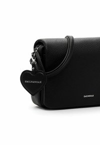 Bandolera de cuero negro con superficie texturizada, borde curvado y cierre de cremallera. Presenta un charm en forma de corazón con el logotipo "EMILY & NOAH".