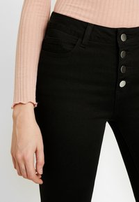 Jeans negros de cintura alta con un cierre de cinco botones, que cuentan con una textura suave, costuras sutiles y un diseño clásico de cinco bolsillos.