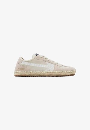 Lage beige sneaker met geweven juten zool, witte gestructureerde zijstreep, veters en ACBC-logo nabij de hiel op witte achtergrond.