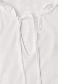 Haut en tissu blanc avec un décolleté en V et de fines cordelettes à nouer au col, présentant un bord délicatement volanté.