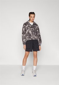 Pullover grigio camouflage con zip a quarti, abbinato a pantaloni cargo neri. L'outfit è completato da sneaker grigie e calzini bianchi.